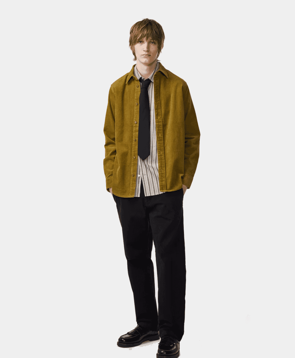 Model wearing a mustard corduroy overshirt over a striped button-up with black trousers.