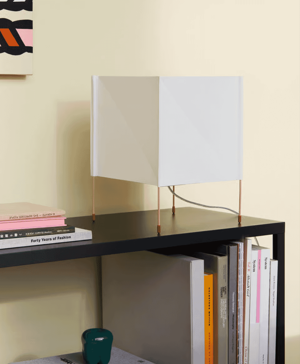 A minimalist white table lamp with copper legs on a bookshelf.