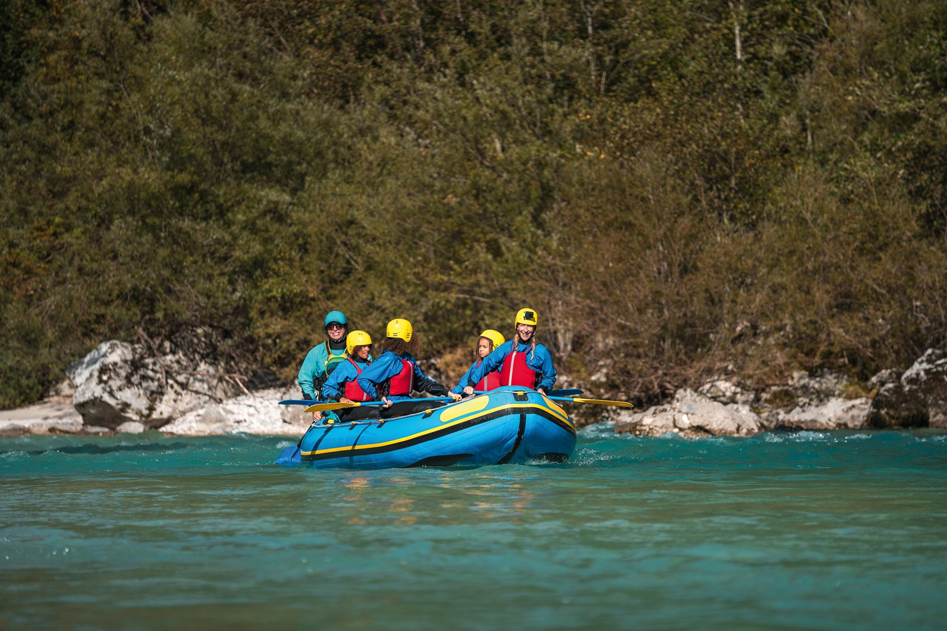 A group of people navigating a turquoise river in a white-water raft.