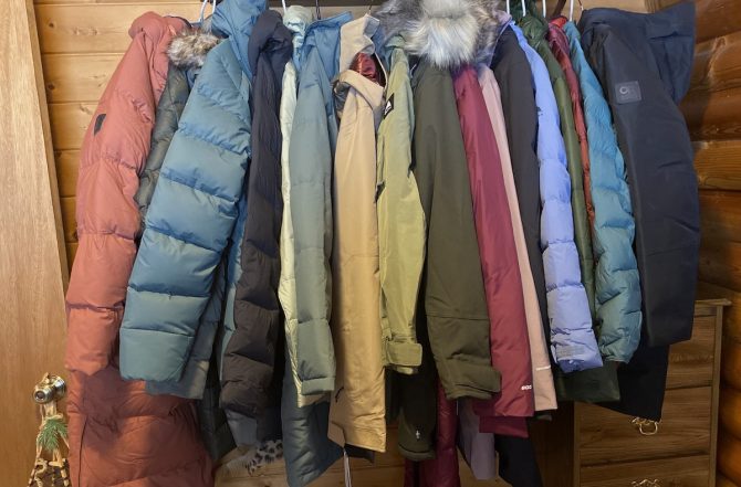 A row of various colorful winter parkas hanging on a rack inside a cabin.