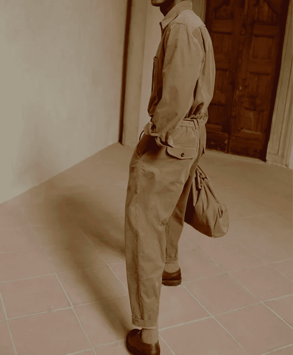 Man in a relaxed-fit corduroy utility jumpsuit with rolled sleeves standing in a studio.