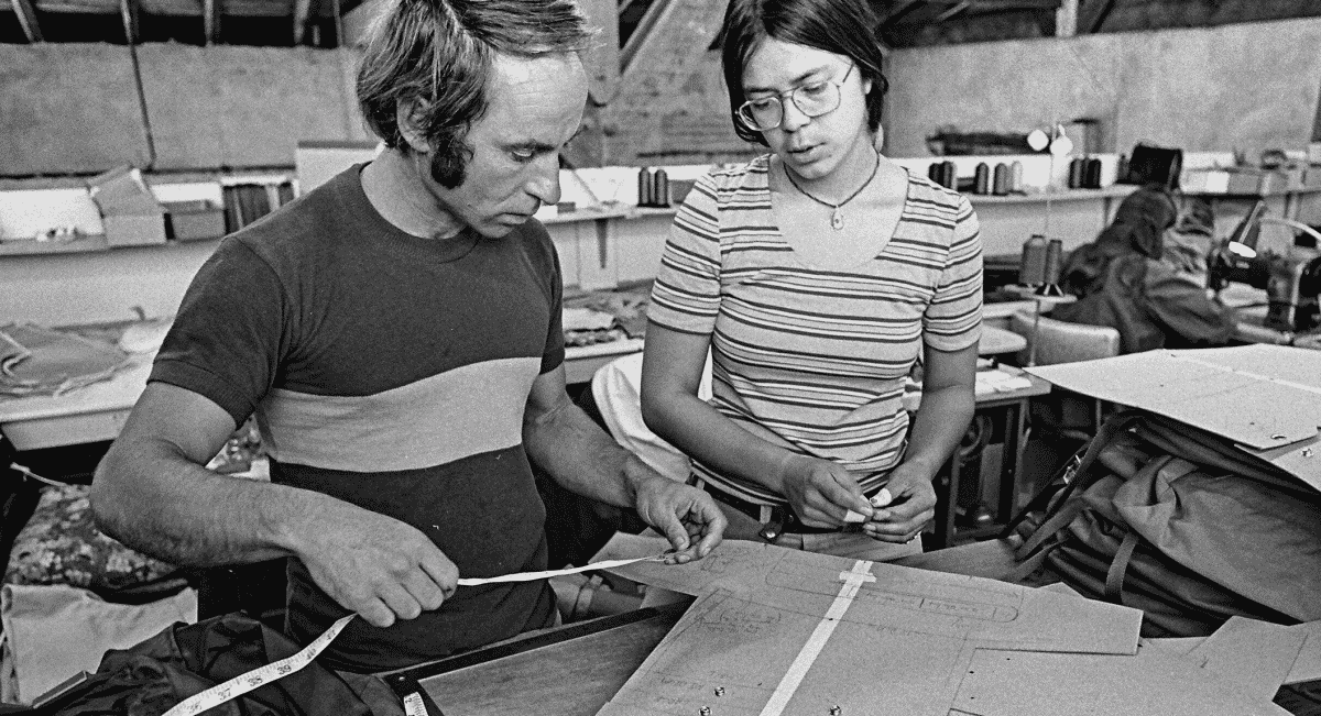 Two people in a workshop examining garment patterns surrounded by fabric.