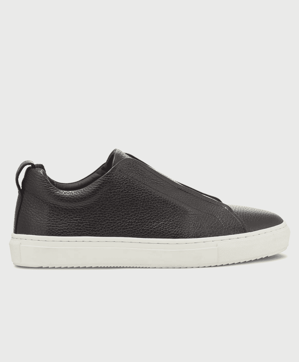 Side profile of a black pebbled-leather slip-on sneaker with a white sole.