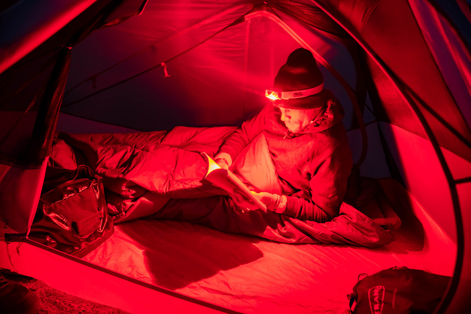 The interior of a tent illuminated by the soft red light of a headlamp.
