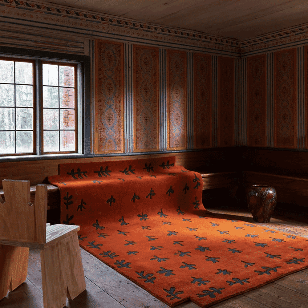 Close-up of a vibrant orange patterned rug in a rustic room with wooden furniture.