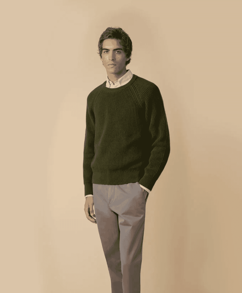 Man wearing a forest green ribbed sweater over a white shirt with gray trousers.