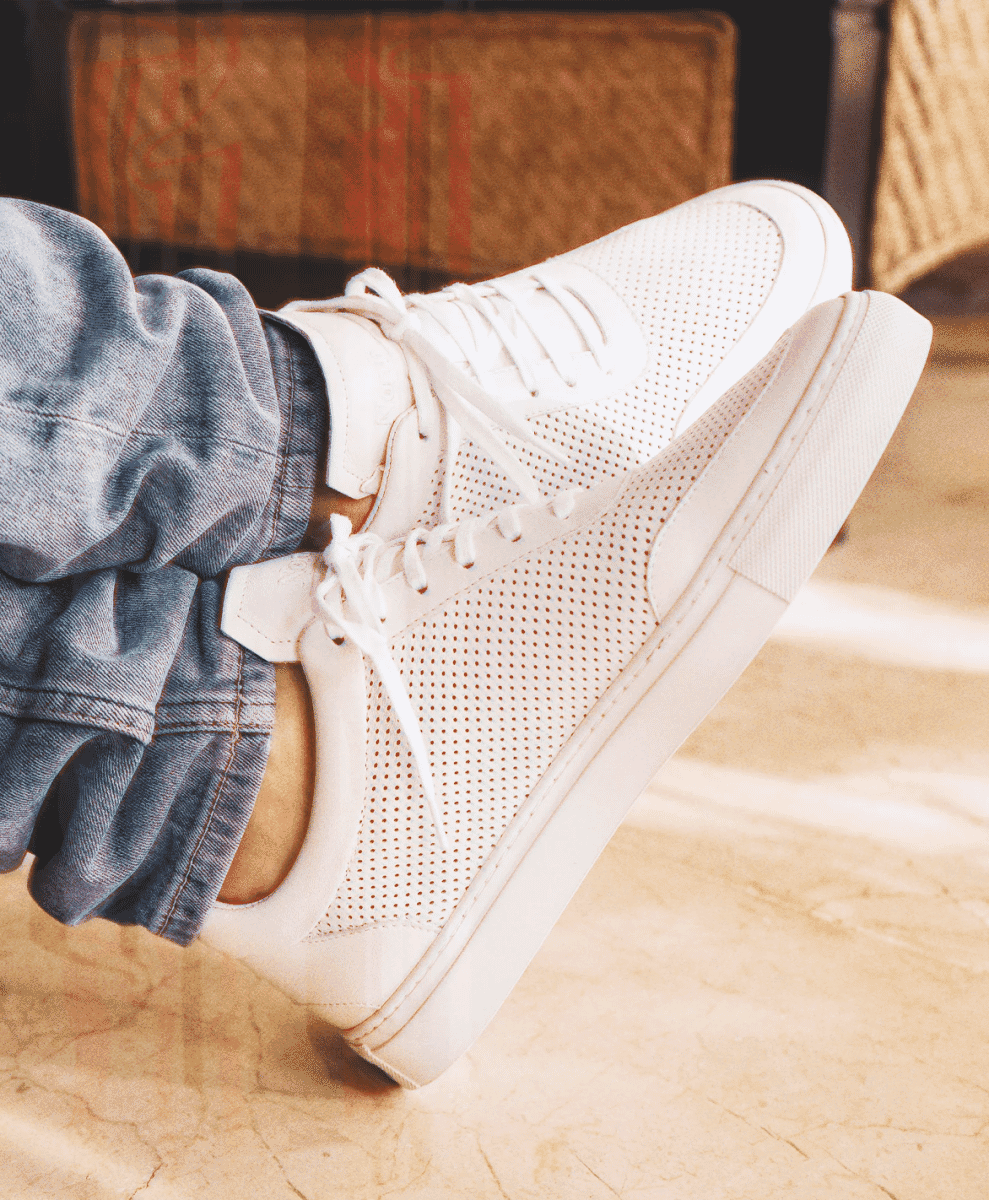 Close-up shot of a person wearing white perforated sneakers with light-wash denim jeans.