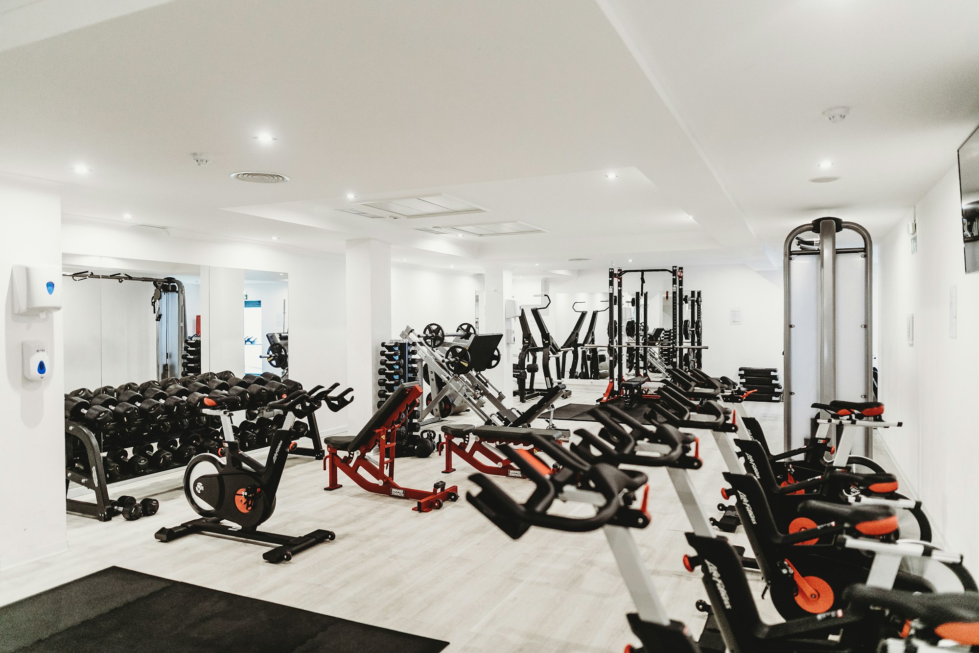 A modern home gym interior featuring a sleek soundbar mounted on the wall beneath a mirror.