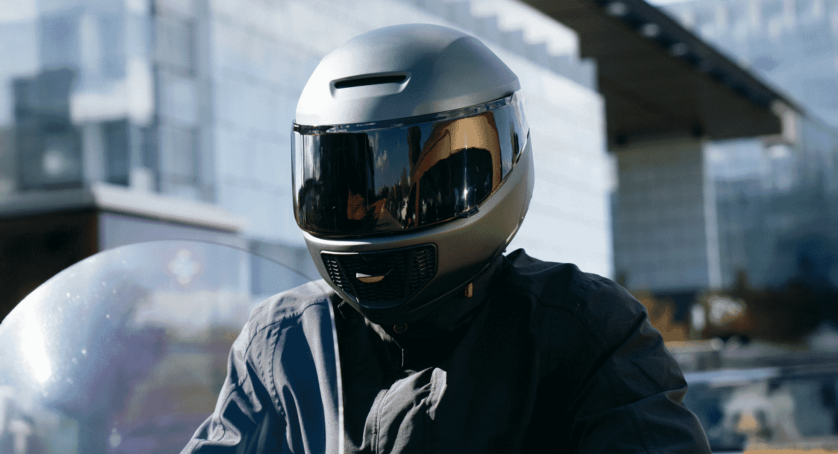 Motorcyclist in a silver helmet and dark jacket riding in an urban setting