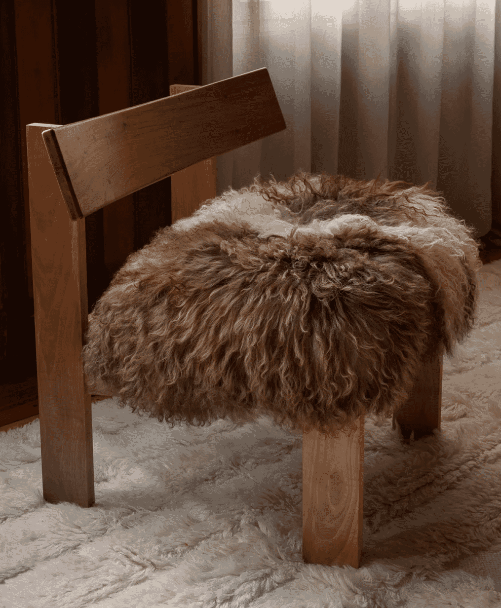 A rustic wooden stool draped with a fluffy sheepskin cushion.