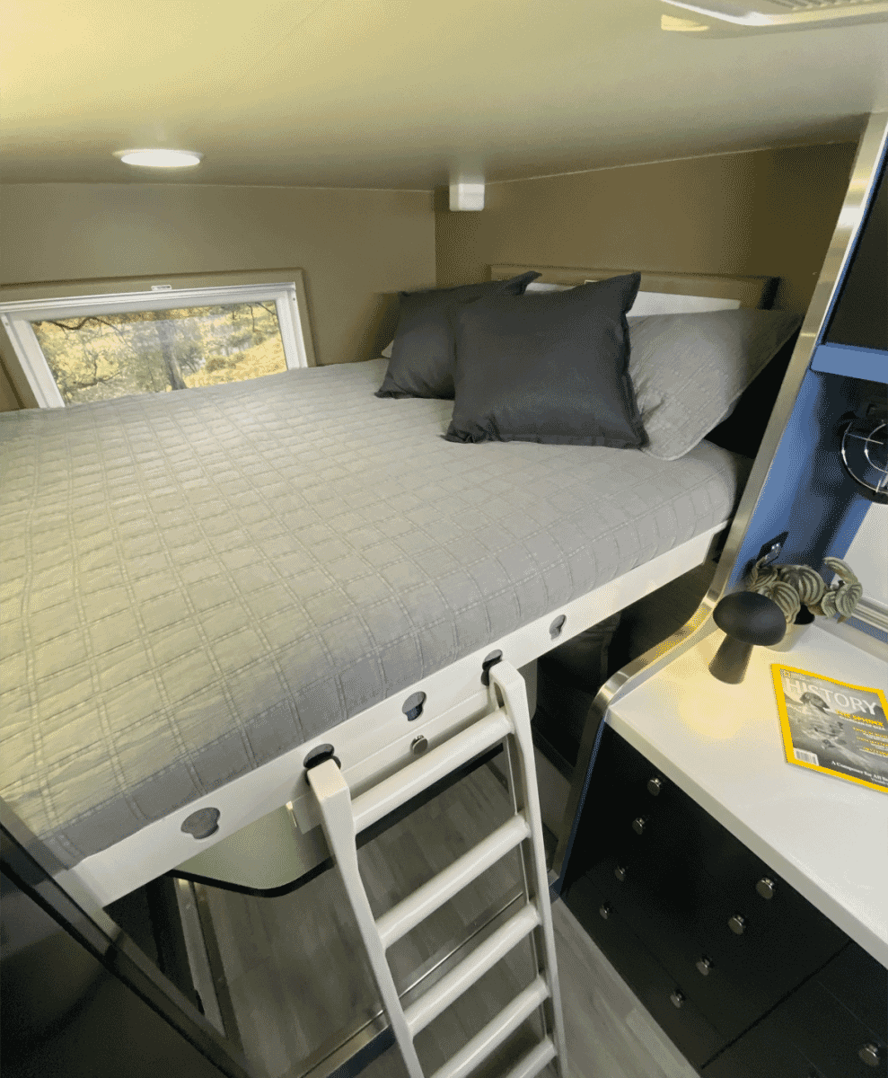 Interior view of the camper's loft bed area featuring modern gray bedding and a minimalist ladder.