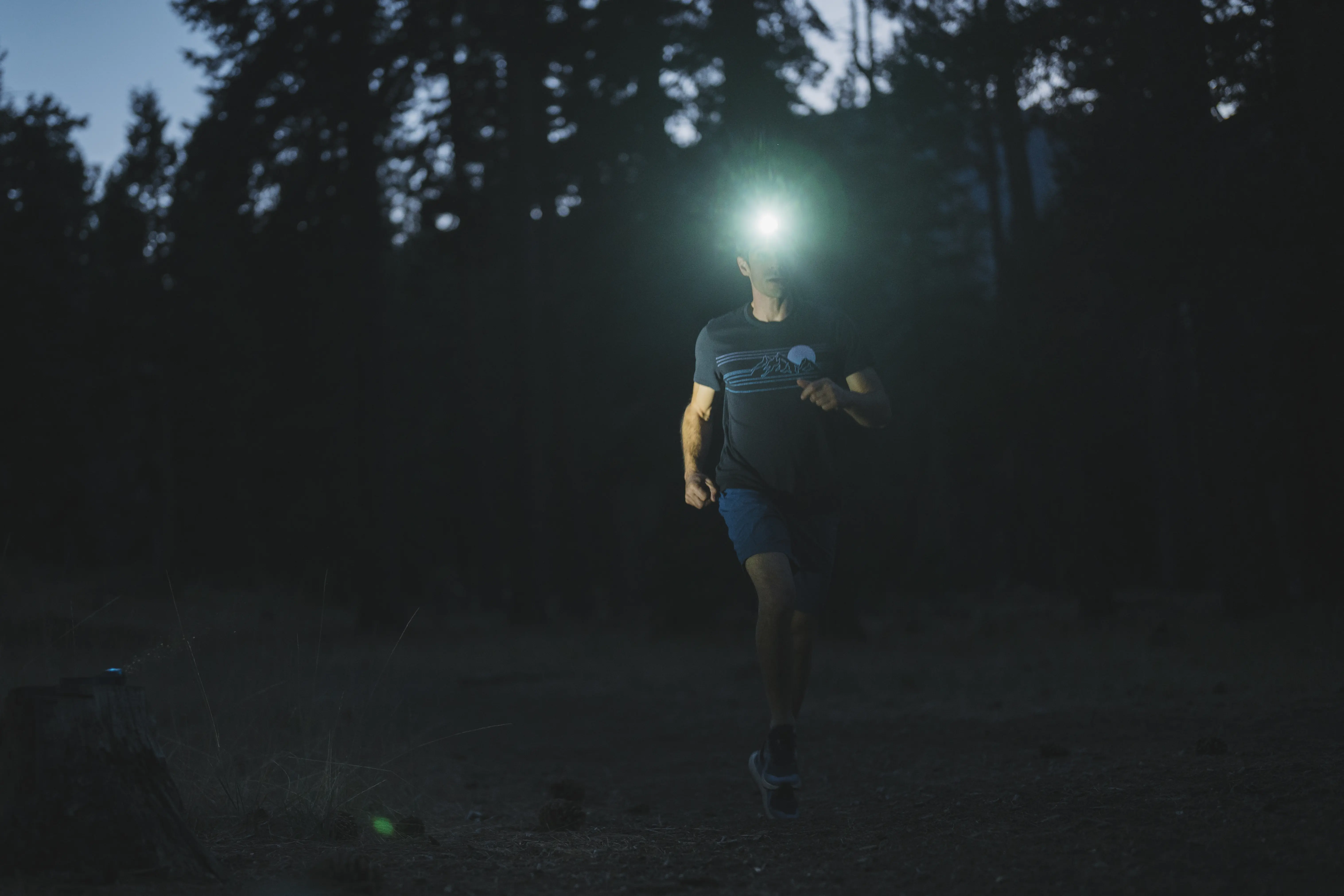 A trail runner using a headlamp during a dusk run on a dirt path.