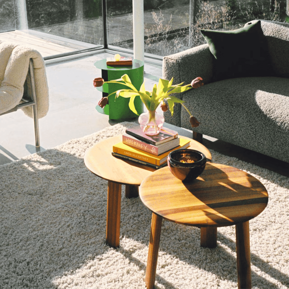 A modern sunlit living room with a textured gray sofa and clean wooden coffee tables.