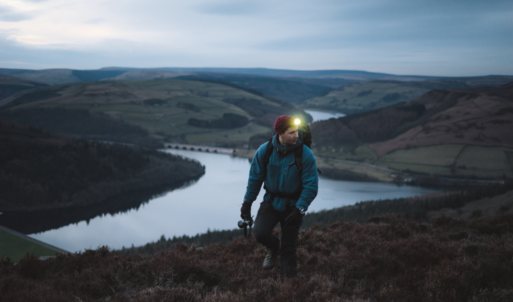 A hiker using a powerful headlamp to illuminate a dark forest trail at night.
