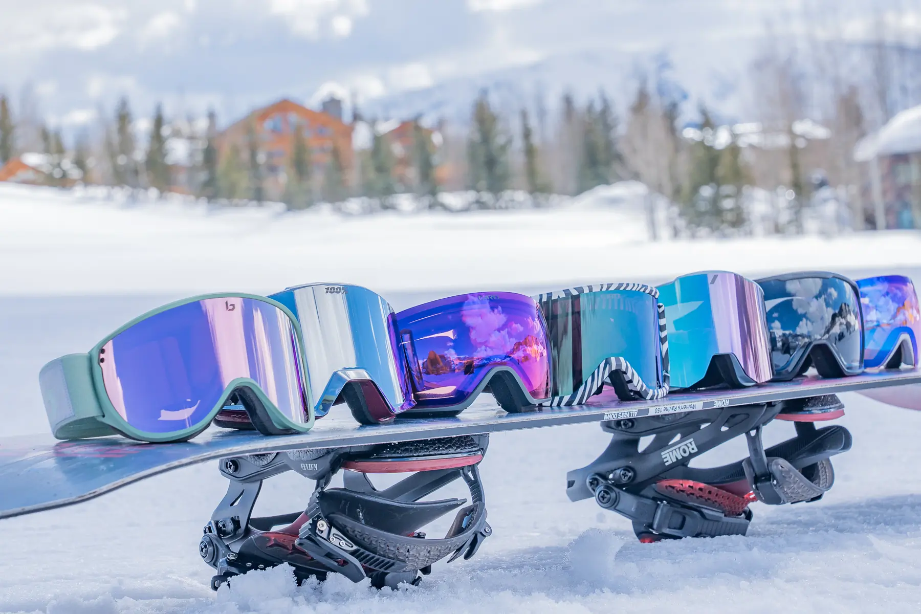 Several pairs of ski goggles resting safely on a snowboard at a ski resort.