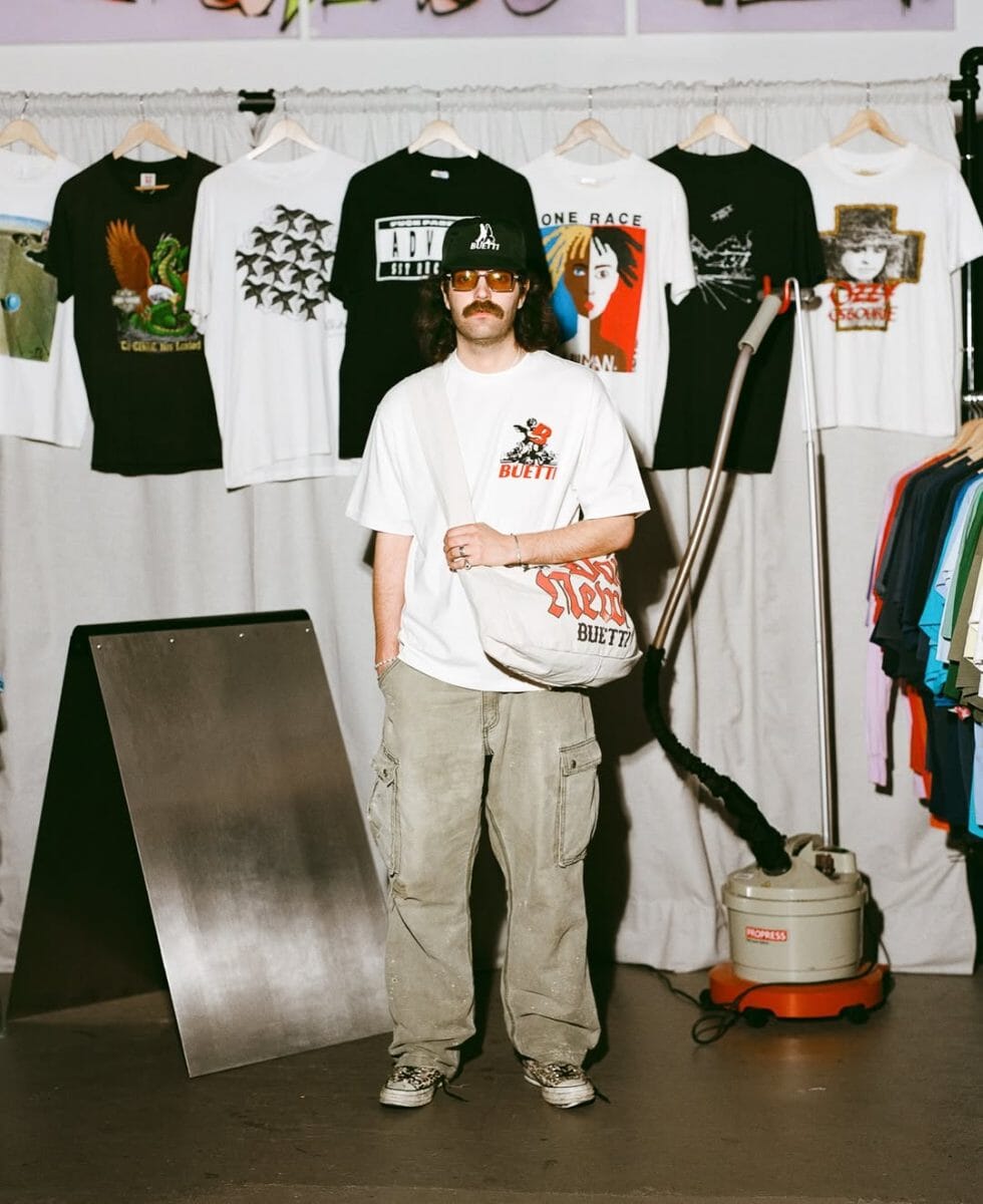 Man with sunglasses wearing a white graphic T-shirt and black baseball cap.