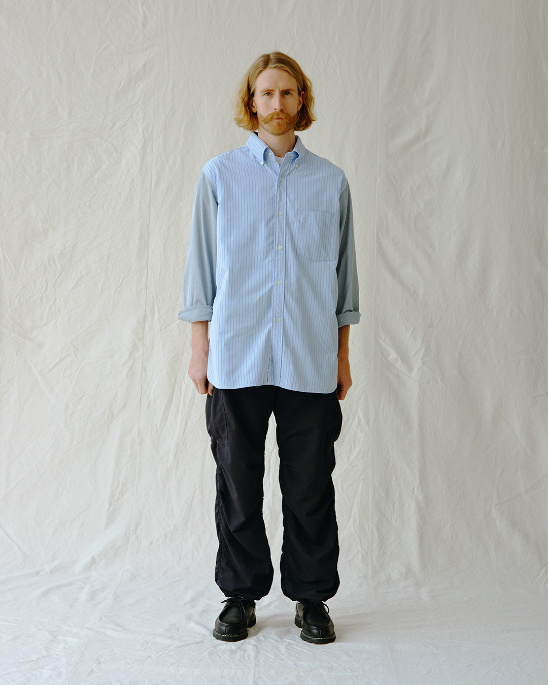 Man wearing a light blue striped shirt with contrasting grey sleeves.