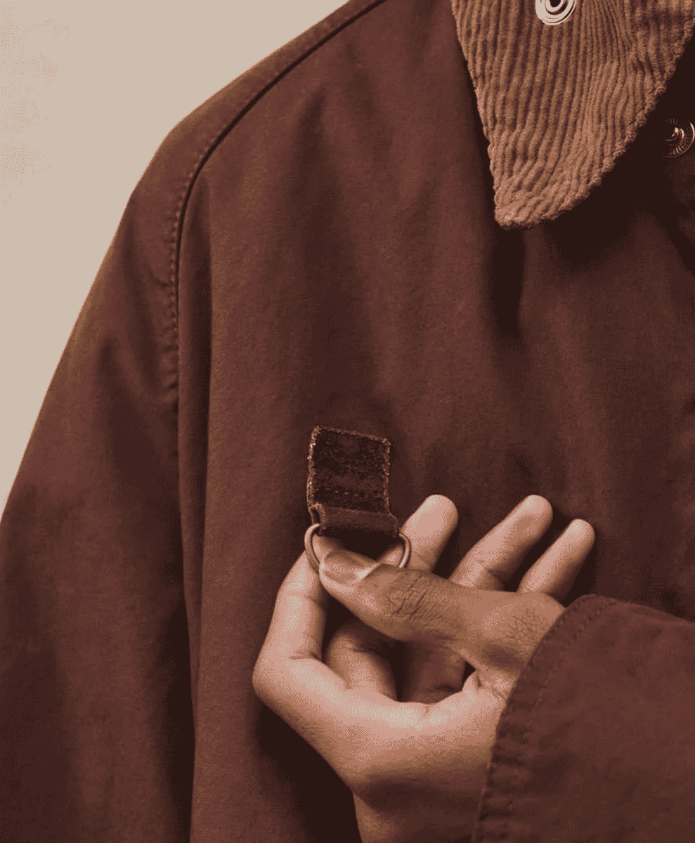 Close-up of a brown corduroy collar and leather strap detail on a waxed jacket.