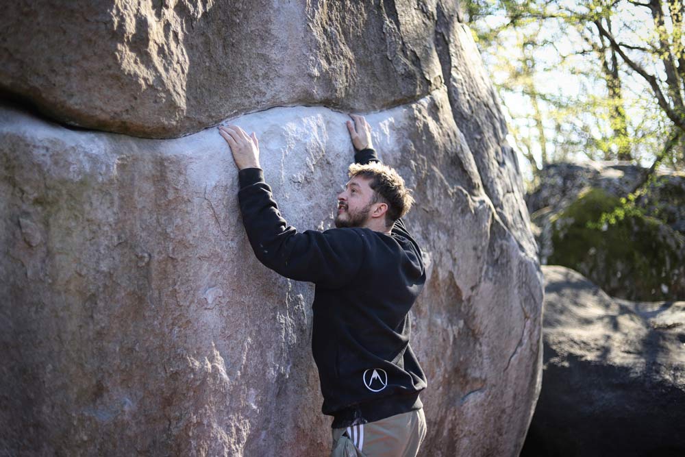 A climber reaching into a chalk-heavy crack on a large boulder outdoors
