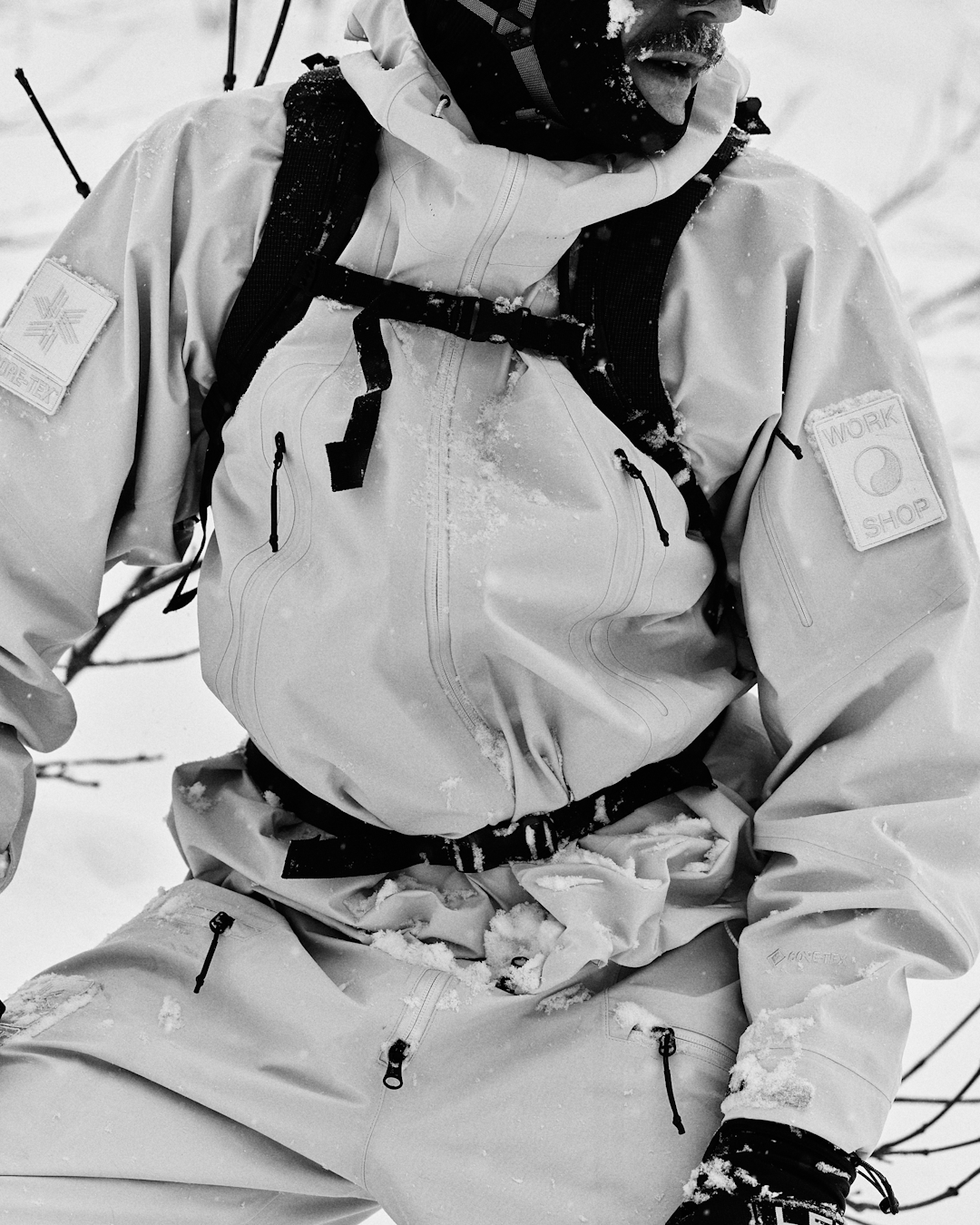 Man in a light Gore-Tex jacket with a 'WORK SHOP' patch standing in a snowy landscape.