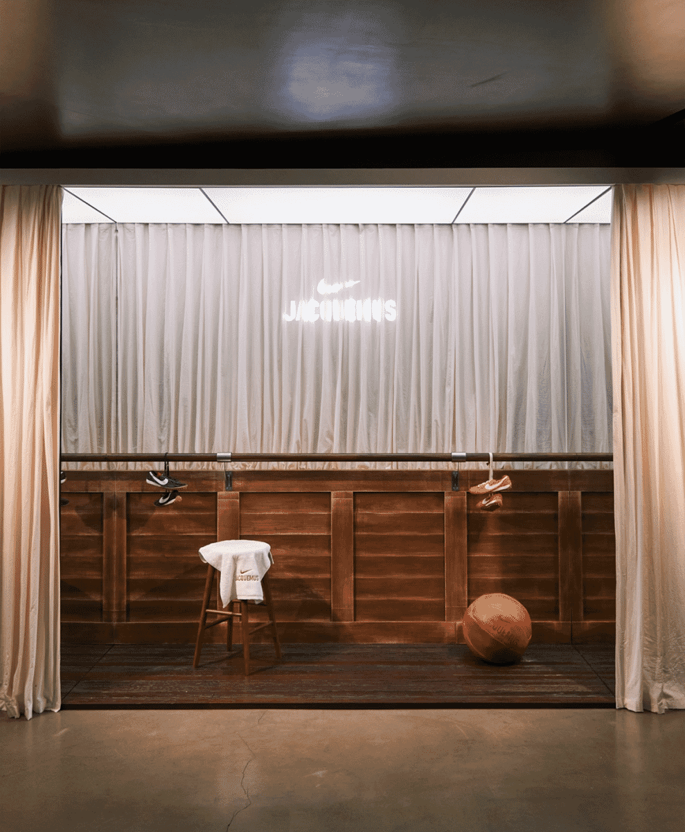 A curated display featuring Nike x Jacquemus sneakers and apparel on a wooden stage with curtains.