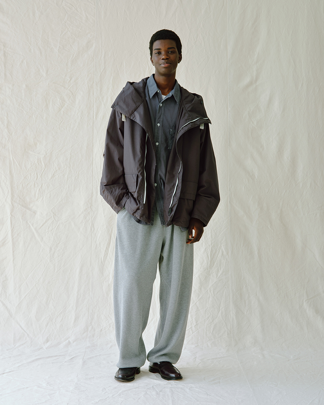 Oversized dark gray hooded jacket paired with loose gray sweatpants.