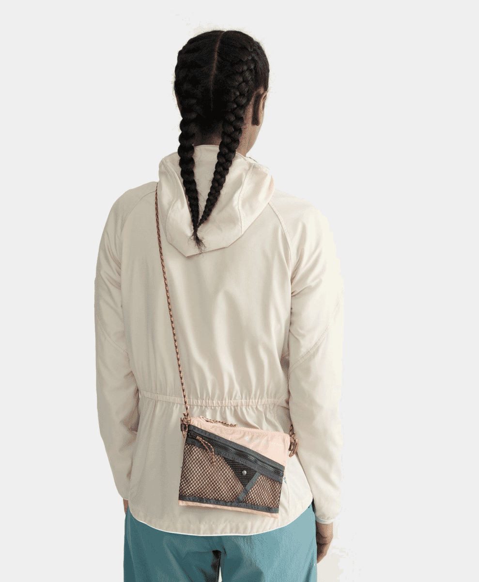 A person wearing a cream jacket and teal trousers with a mesh crossbody bag.