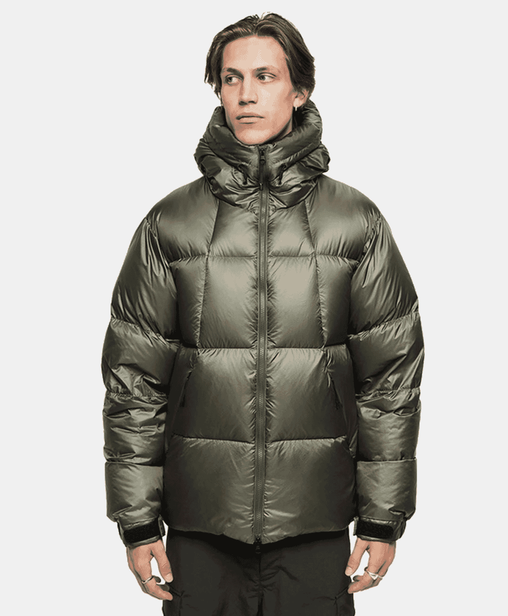 Model in a dark olive green puffer jacket with a high collar and quilted design.