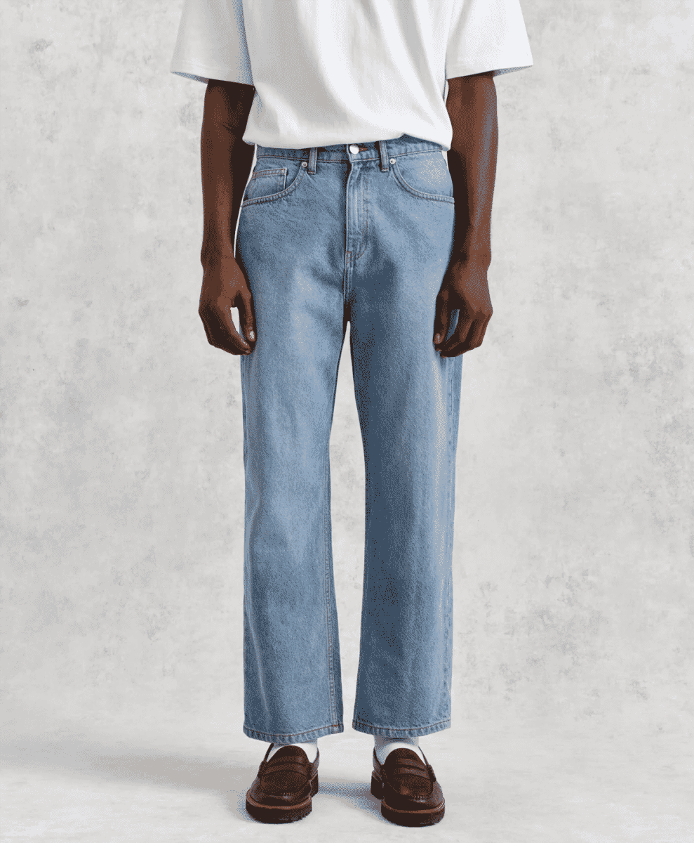 A model in light-wash wide-leg denim jeans and a white t-shirt against a gray background.