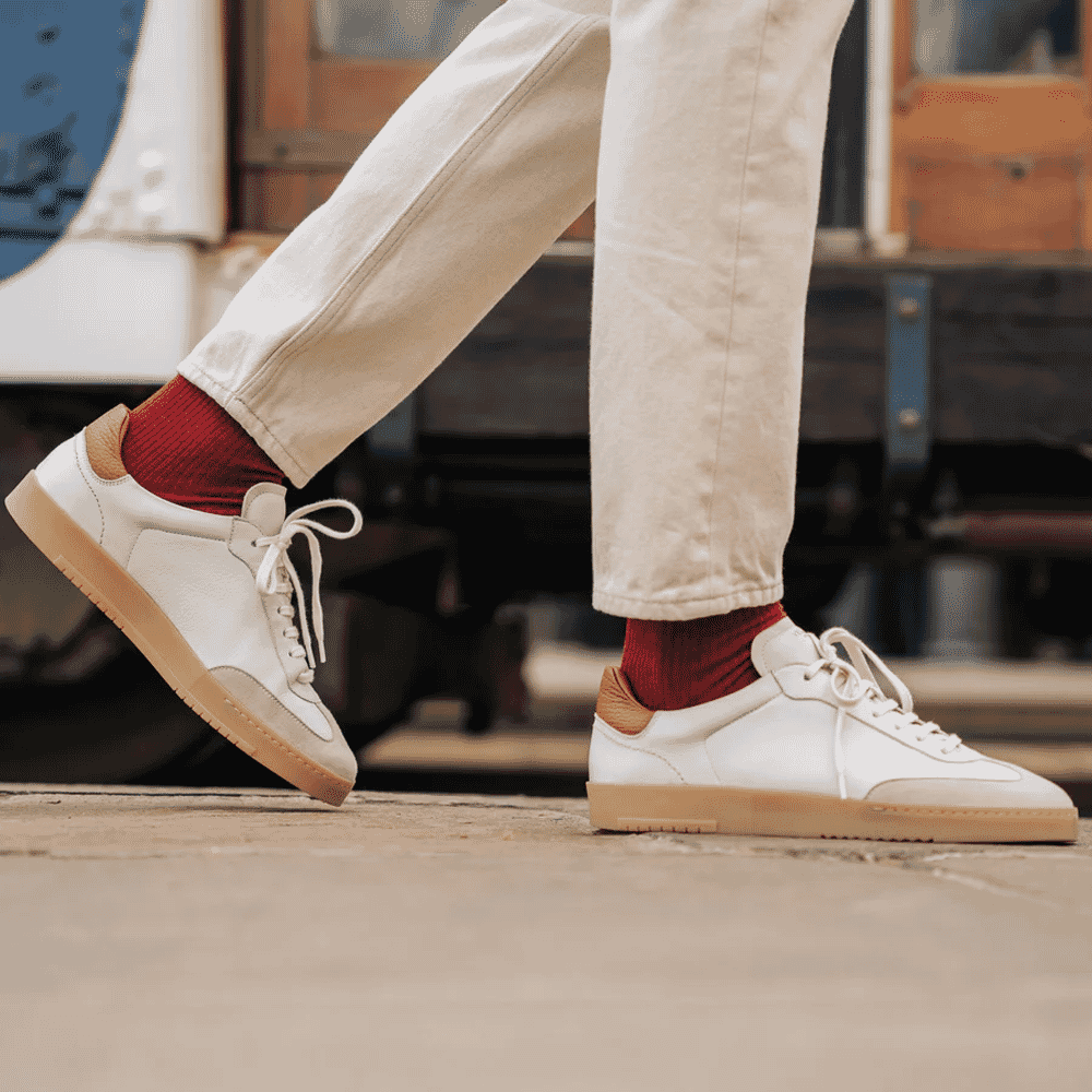 A man in cream trousers and red socks wearing white leather sneakers mid-step.