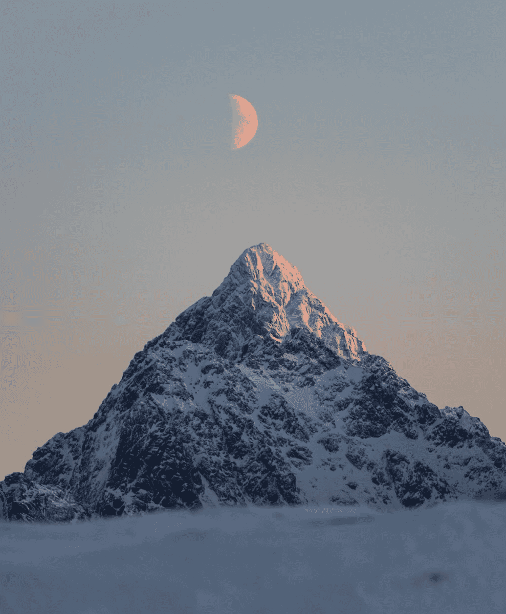 A snow-capped mountain peak under a twilight sky with a visible crescent moon.