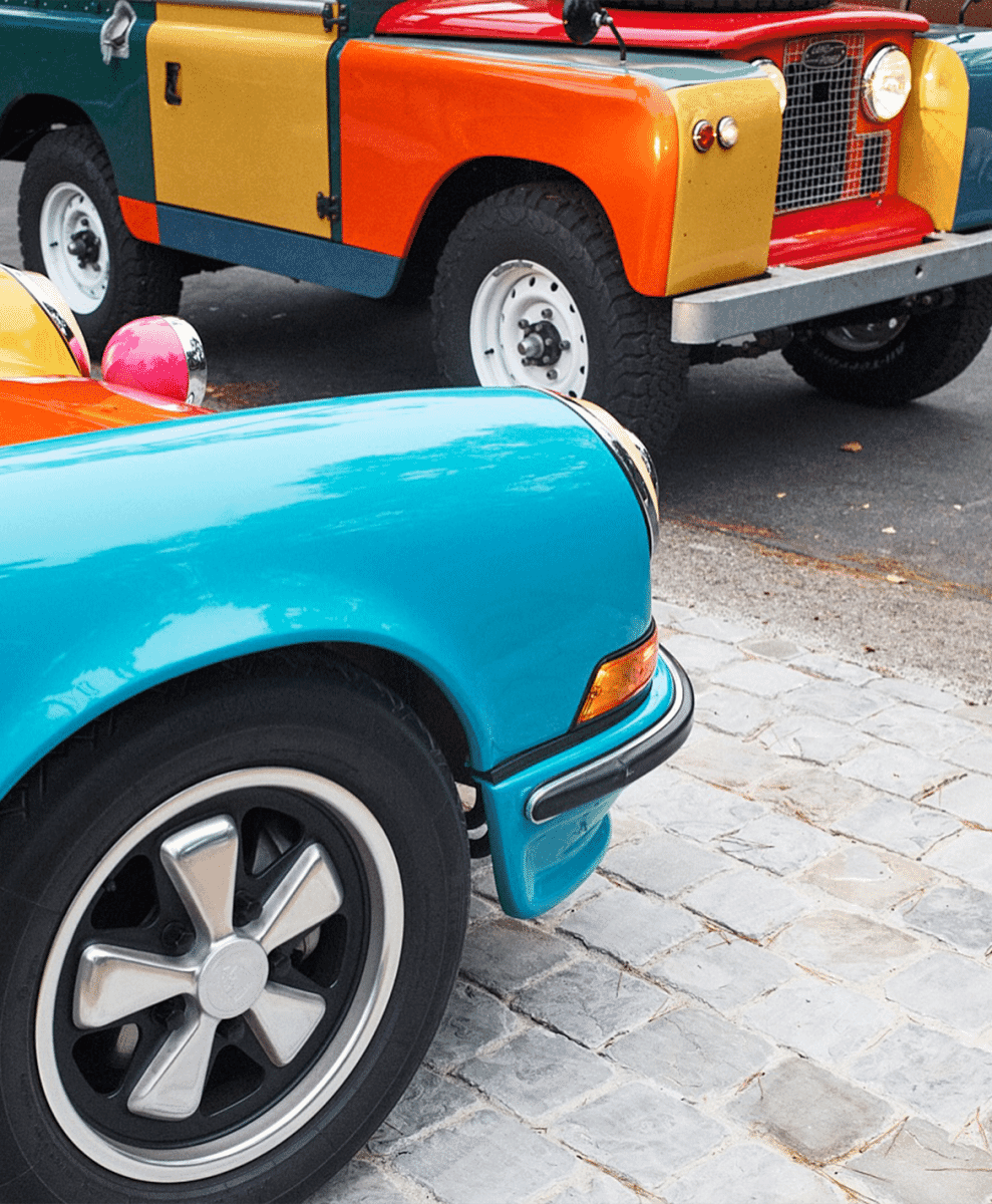 A turquoise Porsche and a multicolored Land Rover parked on a cobblestone street.