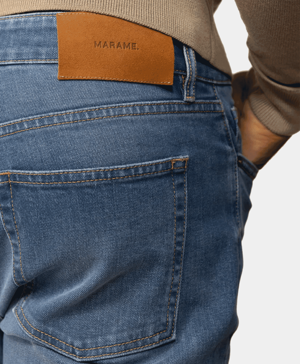 Close-up of blue denim jeans featuring a tan leather brand patch and a beige ribbed sweater.