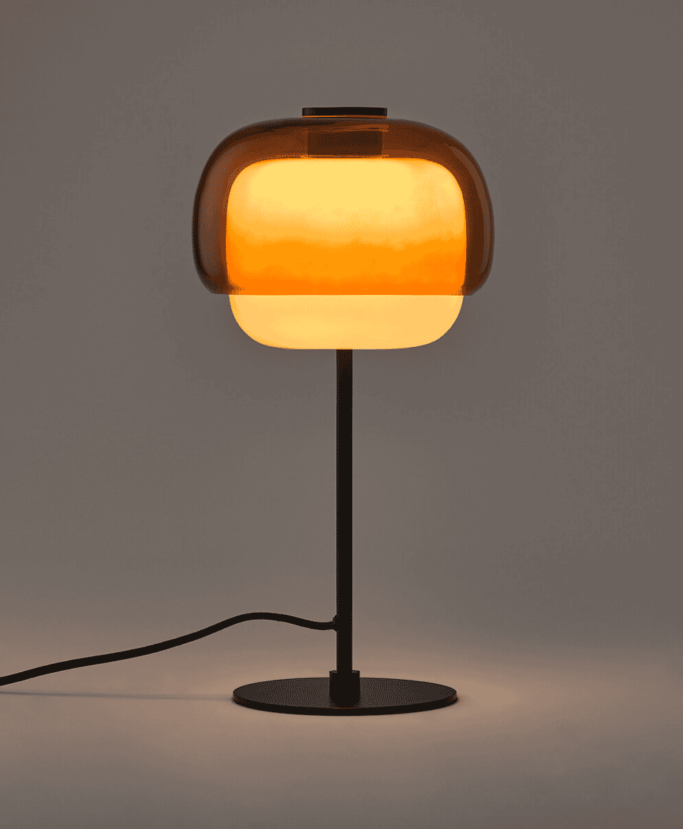 Minimalist table lamp with a translucent amber glass shade and a black metal base emitting a warm glow.