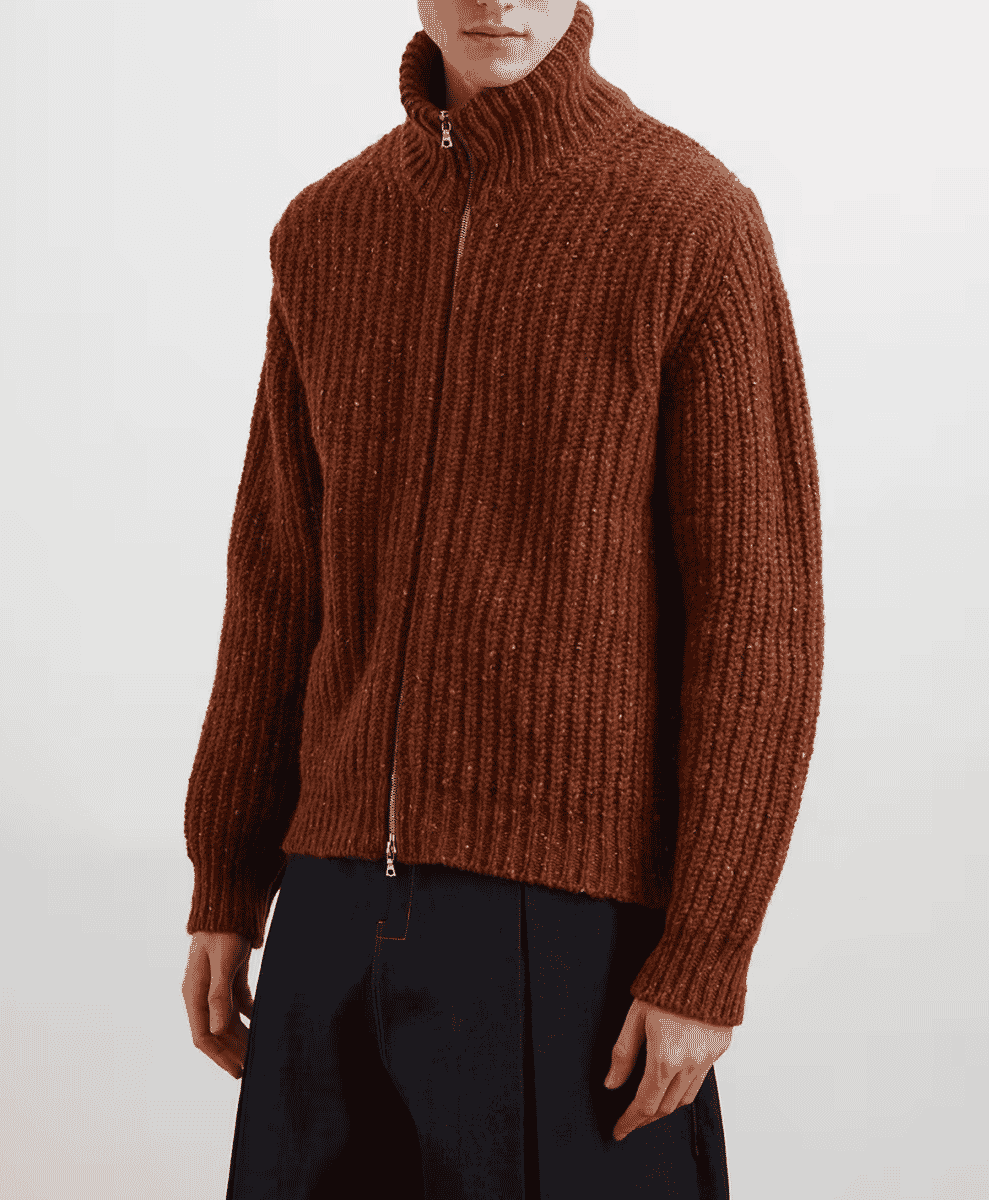 Male model in a chunky brown ribbed knit zip-up sweater with a high collar and dark trousers.