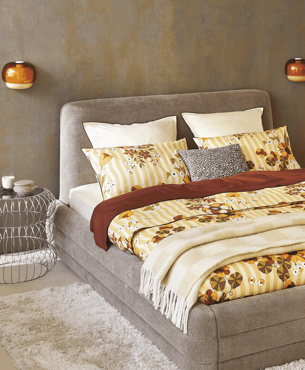 Cozy bedroom featuring autumn-toned floral bedding and warm, soft-glow wall sconces.