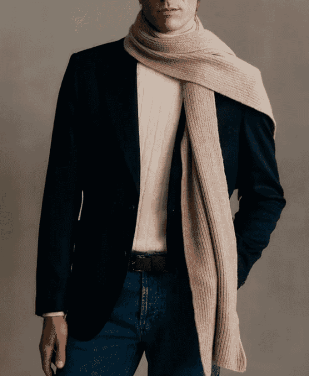A man modeling a black blazer, cream ribbed turtleneck, and a matching oversized scarf.