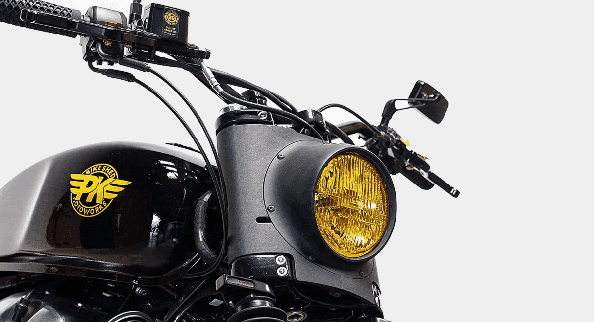 Close-up of the custom yellow-tinted headlight and PK Motoworks logo on the black fuel tank.