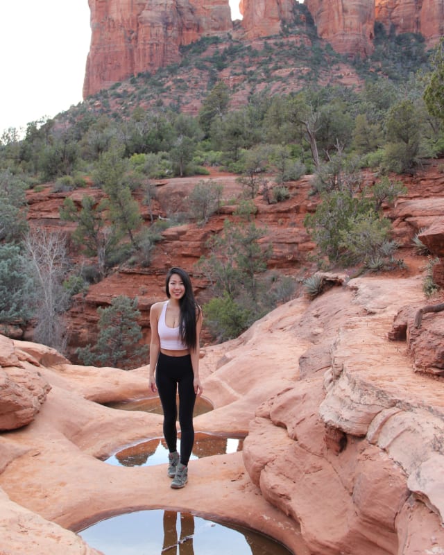 A woman hiking across red rock formations wearing flexible black leggings.