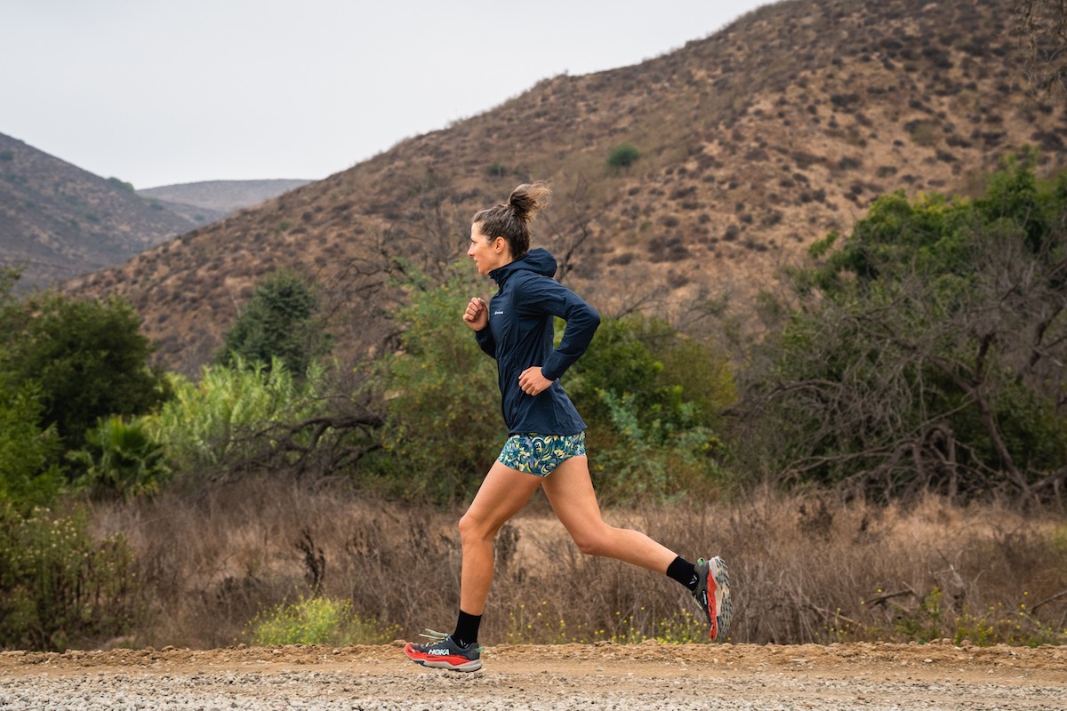A runner mid-stride on a technical desert trail wearing Hoka trail shoes.