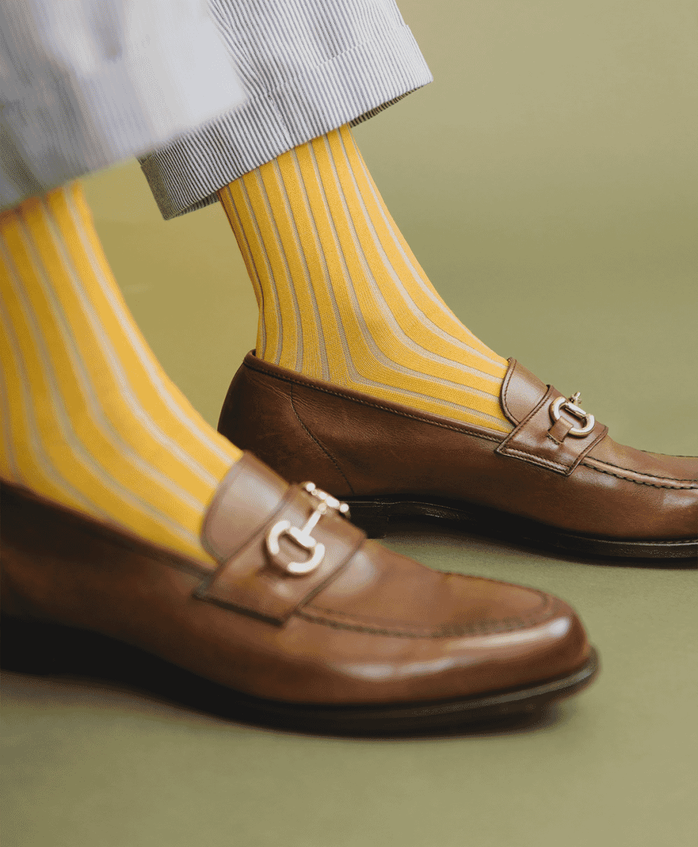 Close-up of yellow striped socks with brown leather loafers and cuffed striped trousers.