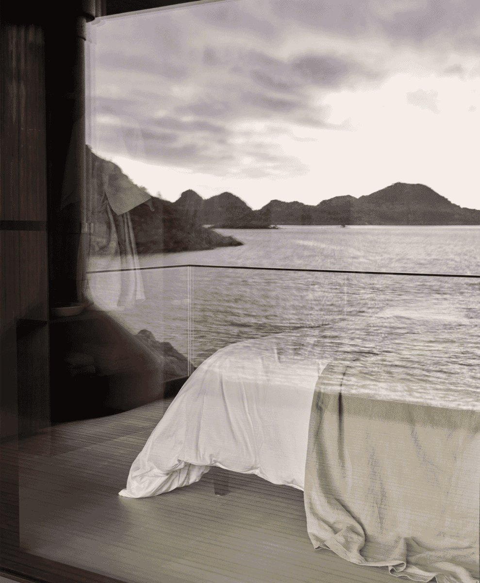 A minimalist bedroom with white linens and large windows overlooking the sea.