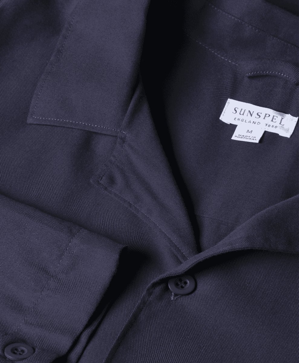 Detail shot of a dark navy shirt collar with a white Sunspel England 1860 woven label.