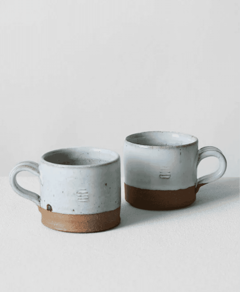 Two handmade ceramic mugs with white glaze and brown clay bases.
