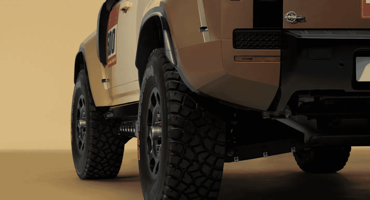 Close-up of the oversized off-road tires and rugged suspension on a beige rally vehicle.
