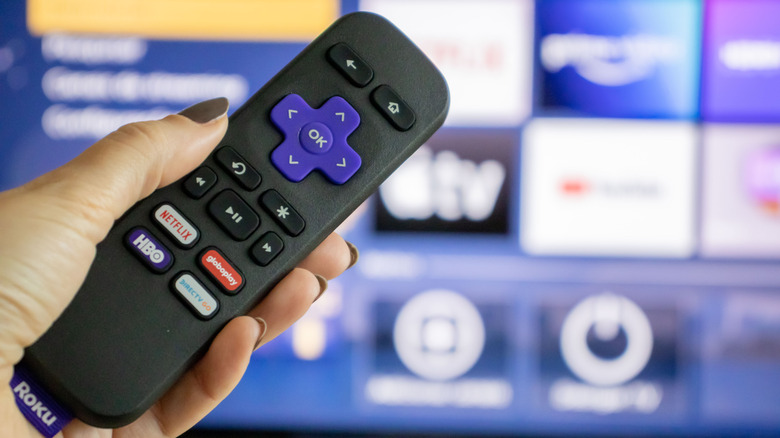 A person holding a Roku remote pointing it at a smart television.