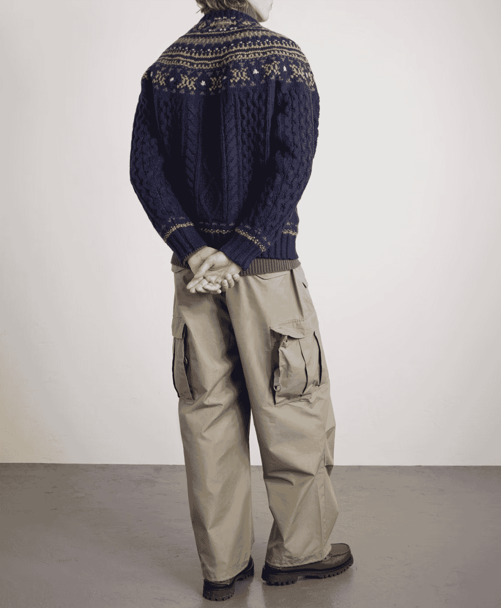 Rear view of a man wearing a navy blue Fair Isle cable-knit sweater with cargo pants.