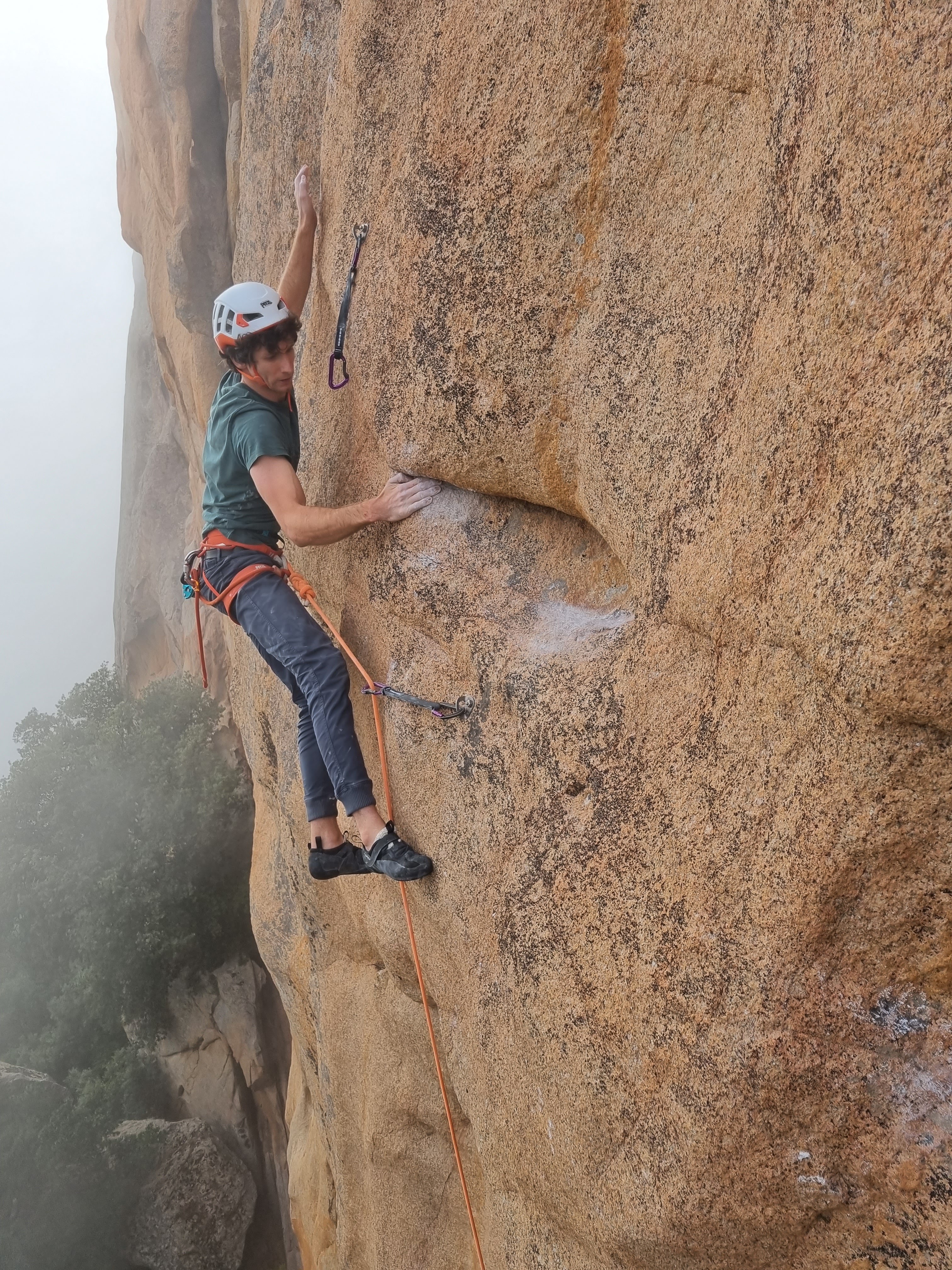 A climber clipping a quickdraw into a bolt while sport climbing on granite.