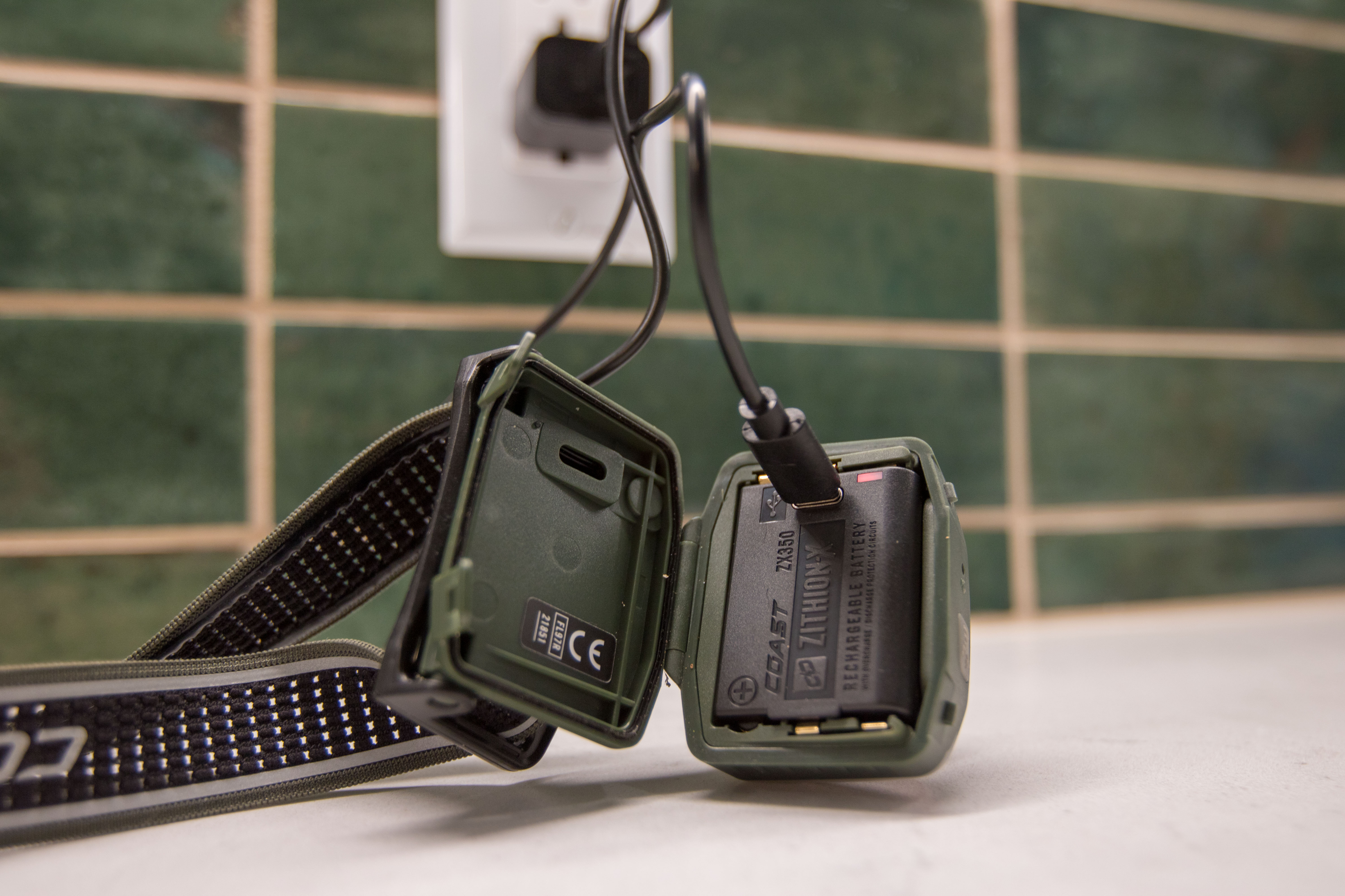 A disassembled Coast headlamp with a USB-C cable charging its lithium-ion battery.