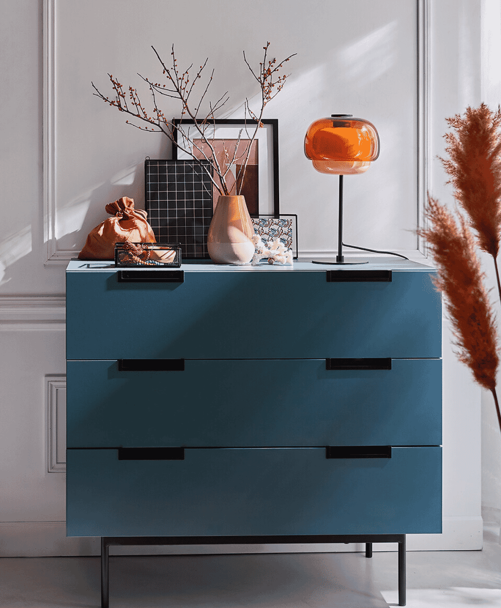 Modern teal dresser styled with a bright orange dome-shaped lamp and minimalist decorative objects.